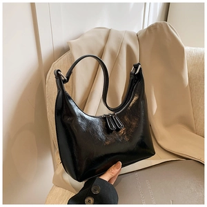 Dettaglio borsa hobo nera lucida con cerniere argento appoggiata su un blazer beige