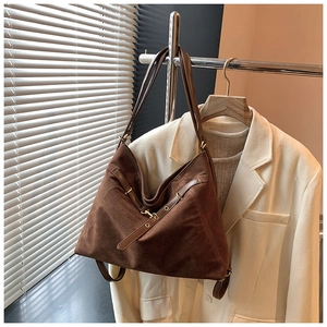 Detail of dark brown faux suede tote bag hanging next to a beige blazer in soft light