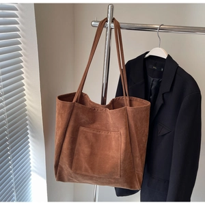 Detailed view of brown faux suede tote bag with front pocket hanging in a modern studio