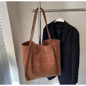 Detail view of large brown faux suede tote bag with front pocket hanging in a stylish setting