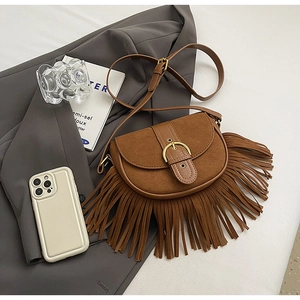 Detailed close-up of brown suede saddle bag with golden horseshoe buckle and fringe