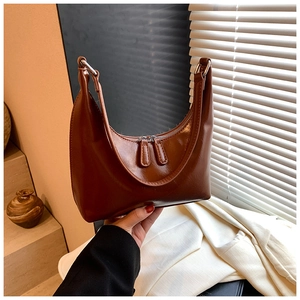Dettaglio della trama di una borsa a mezzaluna marrone in ecopelle lucida con zip argento