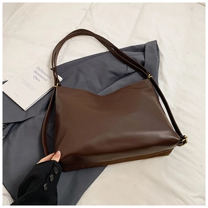 Detail of a dark brown large leather tote bag with matte finish and gold metal buckles