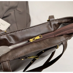 Detailed close-up of dark brown vintage leather tote with metal zipper and striped lining