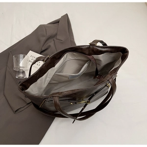 Detail view of large dark brown leather tote bag with gray lining and zipped inner pocket