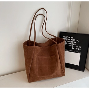 Close-up of a large brown suede tote bag featuring a square front pocket and slim straps
