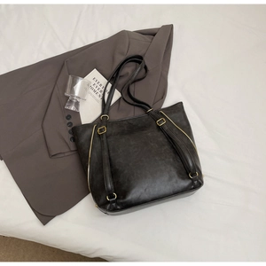 Close-up of black retro tote bag with golden hardware and side zipper on grey blazer