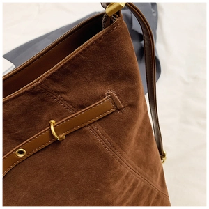 Close-up of brown suede shoulder bag showing metal ring buckle and leather strap details