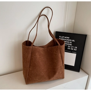 Detail of minimalist dark brown suede tote bag with slim shoulder straps in a clean studio setting