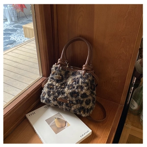Dettaglio della borsa in peluche leopardata con manici in pelle marrone su base di legno