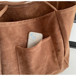 Detail of suede tote bag front pocket showing phone storage and fine stitching work