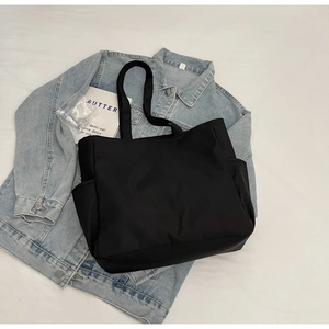 Vue à plat du fourre-tout noir minimaliste avec poches latérales sur veste en jean