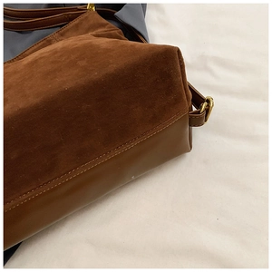 Close-up of brown suede and leather stitching with gold metal adjustment buckle on tote