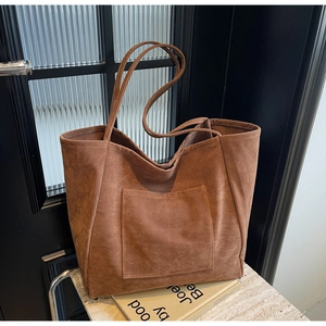 Detail view of brown faux suede tote bag with large front pocket on marble surface