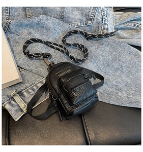 Close-up of black lychee grain mini bag with metal carabiner and woven strap details