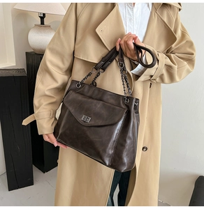Dettaglio borsa tote marrone con chiusura a scatto e tracolla a catena su un trench