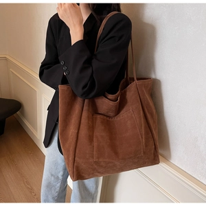 Detail of large brown suede tote bag featuring a spacious front pocket and long shoulder strap