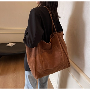 Brown suede tote bag with front pocket shown on shoulder in a minimalist urban setting