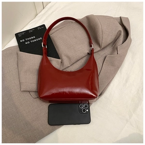 Dettaglio di una borsa sottobraccio a mezzaluna rosso scuro lucido con smartphone incluso
