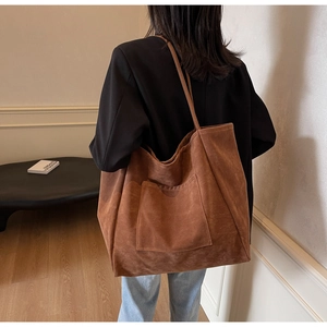 Detail of a large brown suede tote bag featuring a front pocket and long shoulder straps