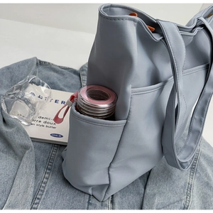Détail d'un sac cabas en nylon bleu avec poche latérale et gourde sur un jean foncé