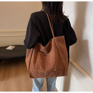 Detail of a large brown suede tote bag featuring a square outer pocket and slim shoulder strap