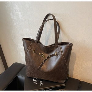 Close-up of vintage brown leather tote bag with bronze zipper and decorative strap detail