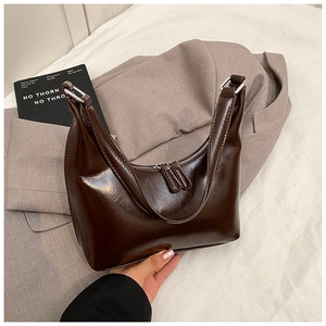 Dettaglio di una borsa a mezzaluna in pelle marrone scuro lucida con doppie zip argentate
