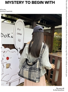 Stylishly oversized black and white plaid wool tote bag worn by a model at an outdoor cafe