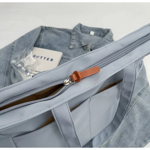 Détail du sac cabas bleu clair montrant la fermeture éclair et la tirette en cuir marron
