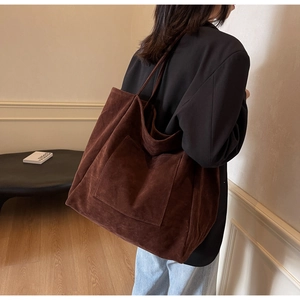 Large dark brown suede tote bag with front pocket shown on shoulder in lifestyle scene