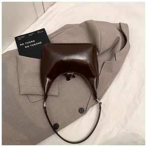 Dettaglio borsa hobo marrone scuro lucida con cerniera argento su sfondo elegante
