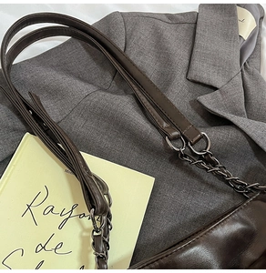 Dettaglio borsa tote in pelle marrone scuro con tracolla a catena e anelli metallici