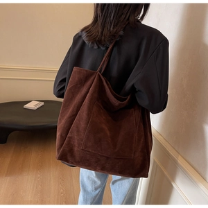Close-up of a large dark brown suede tote bag with a front pocket on a female model