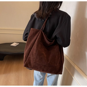Detail of a large dark brown suede tote bag with a functional front pocket on a model
