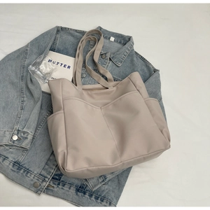 Détail d'un grand cabas en nylon beige avec poches extérieures sur une veste en jean