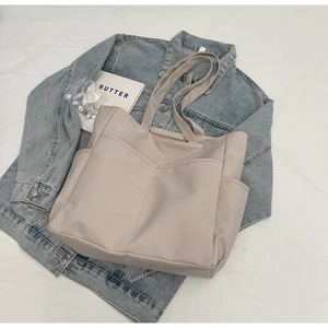 Vue de dessus d'un grand sac fourre-tout beige avec plusieurs poches sur un lit