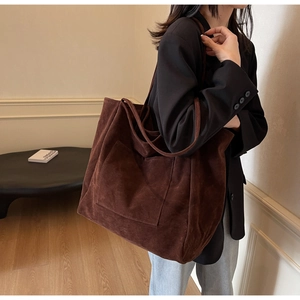Detail of a large brown faux suede tote bag with front pocket shown on a model
