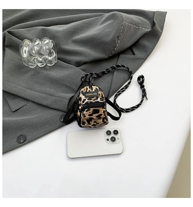 Detailed close-up of a mini leopard print crossbody bag with woven strap and fashion label