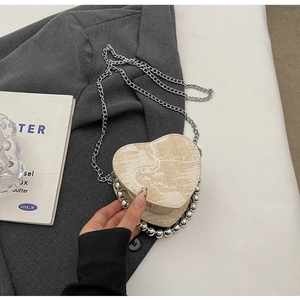 Dettaglio della borsa beige a forma di cuore con perline argentate e tracolla a catena