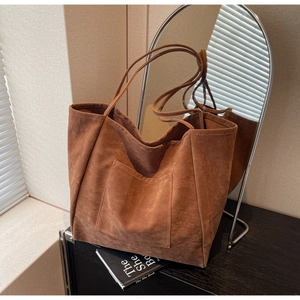 Detail of a large brown suede tote bag featuring a front pocket and slender shoulder straps