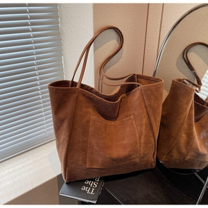 Detail of a large suede tote bag in brown featuring a slim shoulder strap and front pocket