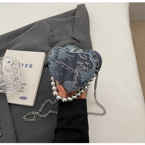 Dettaglio borsa a cuore in denim con manico di perle argentate e tracolla a catena