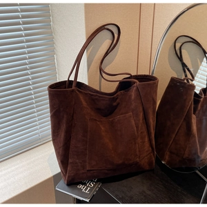 Detail of dark brown suede tote bag featuring a practical outer pocket and slim handles