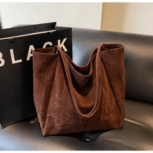 Close-up of a large coffee suede tote bag with front pocket on a black leather sofa