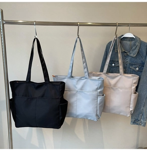 Vue détaillée de sacs fourre-tout en toile noir, gris et beige sur un présentoir en métal
