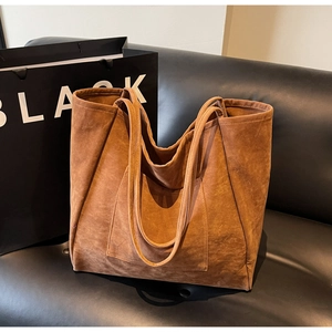 Close-up of brown suede tote bag with front pocket detail on a black leather background
