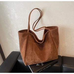 Detail of a large brown suede tote bag featuring a front pocket and long shoulder straps