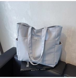 Vue détaillée du sac cabas gris clair en cuir avec plusieurs poches sur un canapé