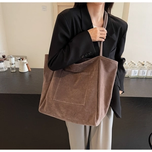 Detail of a large brown suede tote bag featuring a practical front pocket and minimalist style